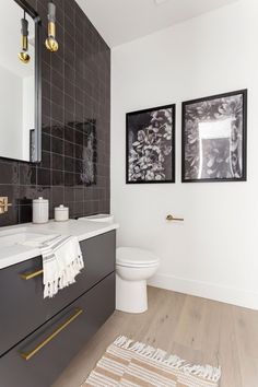 a white toilet sitting next to a bathroom sink under two framed pictures on the wall