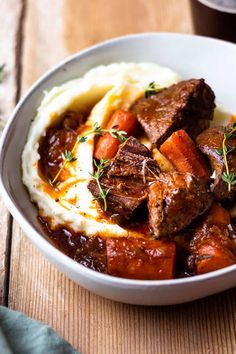 a white bowl filled with meat and mashed potatoes on top of a wooden table