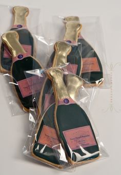 four decorated cookies in the shape of wine bottles with pink and black labels on them