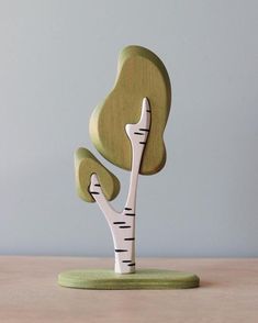 a wooden sculpture of a tree with white and green leaves on the top, sitting on a table