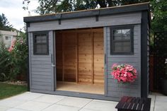 a wooden shed with flowers in the window and on the outside wall, next to a bench