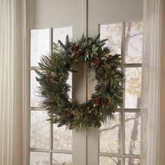 a wreath hanging on the side of a door with pine cones and lights around it