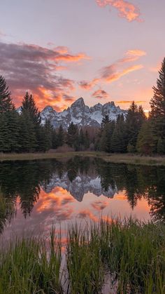 the sun is setting over a mountain range and lake with trees in front of it