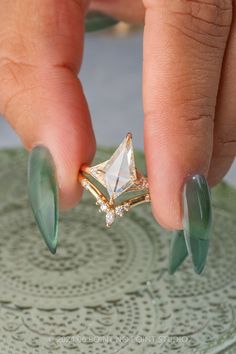 a woman's hand holding a ring with green fingernails