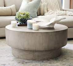 a round coffee table with candles on it in front of a white couch and pillows