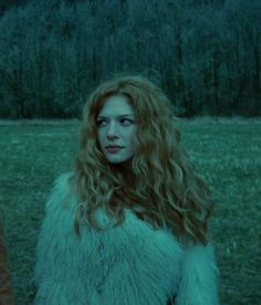 a woman with long red hair standing next to a man in a fur coat on the grass