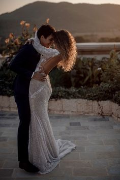 a bride and groom kissing in front of the sun setting on top of a mountain