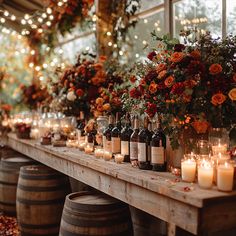 a long table topped with lots of bottles of wine next to candles and flowers in vases