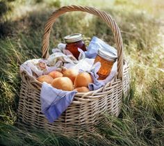 a wicker basket filled with fruit and jams on top of a grass covered field