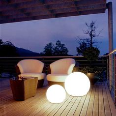 two white chairs sitting on top of a wooden deck next to lamps and a fire place