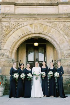 a group of women standing next to each other in front of a building holding bouquets