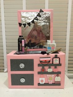 a pink dresser with various items on it and a mirror over the top that is covered in tin foil