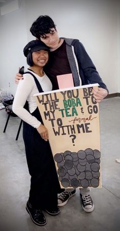 a man and woman standing next to each other holding a sign that says, will you be my tea?