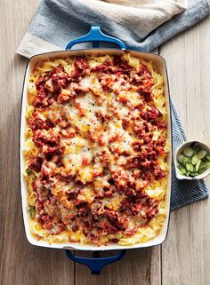 a casserole dish with meat and cheese in it on a wooden table next to a cloth