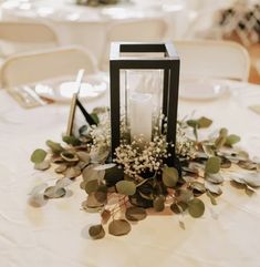 a candle is sitting on top of a table with flowers and greenery around it