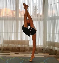 a woman doing a handstand on a yoga mat in front of a window