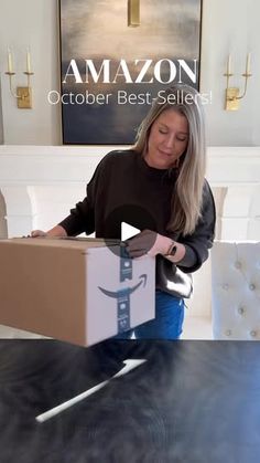 a woman opening a box on top of a table with an amazon sign in the background