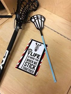 two lacrosse sticks and a sticker on a wooden table next to a racket