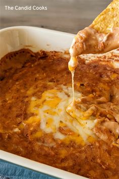 a person dipping some food into a casserole dish with tortilla chips