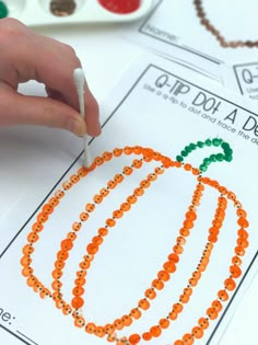 a hand is holding a toothpick over some beads on a sheet of paper