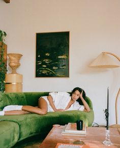 a woman laying on top of a green couch in a living room next to a lamp