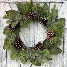 a wreath with pine cones and greenery on a white wooden background, hanging on a wall