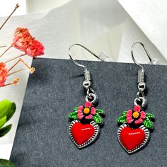 These Dainty Heart Earrings are the ultimate must-have. Expertly handcrafted and exquisitely hand-painted with a bold red enamel finish, playful pink flowers, and vibrant green leaves. Perfect for ladies and girls alike, these adorable dangling heart earrings are an ode to Frida's unique style. A perfect gift for any Fridalover, these Mexican-inspired accents are sure to put a smile on their face. Looking for a charming, one-of-a-kind present that won't break the bank? Look no further than these delightful hand-painted heart earrings inspired by Frida! Each earring is carefully crafted and meticulously painted by hand in our studio, and it takes a considerable amount of time and extreme attention to detail to finish them and finally offer them for sale. “It is always the simple that produc Red Flower Charm Jewelry For Valentine's Day, Heart-shaped Enamel Earrings With Charm, Heart Charm Enamel Earrings, Valentine's Day Heart Charm Enamel Earrings, Red Dangle Flower Earrings For Valentine's Day, Pink Hand Painted Heart Jewelry, Cute Red Hand Painted Jewelry, Cute Hand Painted Red Jewelry, Cute Red Hand-painted Jewelry