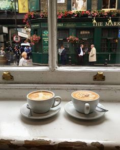 two cups of cappuccino sit on a window sill in front of a store