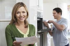 a man and woman are in the kitchen looking at something on the counter top while holding a piece of paper