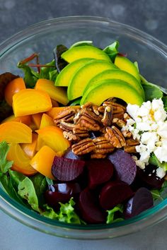 a glass bowl filled with assorted vegetables and nuts, including beets, carrots, avocado, feta cheese and pecans