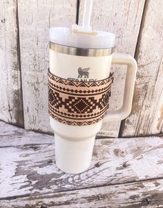 a white coffee cup sitting on top of a wooden table next to a wall covered in wood planks