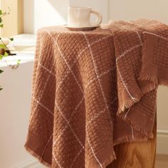 a coffee cup is sitting on top of a table with a brown blanket over it