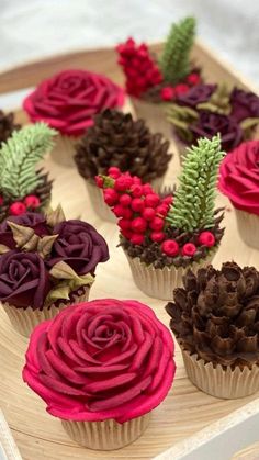 cupcakes decorated with flowers and pine cones on a wooden platter, ready to be eaten