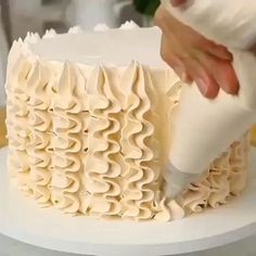 a person is decorating a cake with white icing and ruffles on it