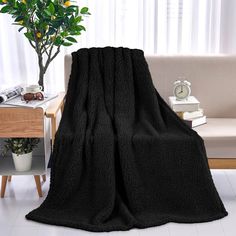 a black blanket sitting on top of a couch next to a table with a potted plant