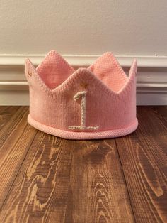 a pink crown with the letter i on it sitting on top of a wooden floor