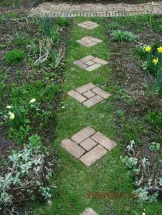 a garden path made out of bricks in the middle of some grass with flowers growing on it