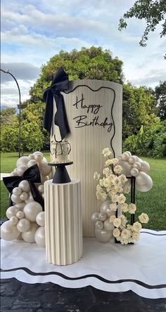 a table topped with vases filled with white flowers and balloon decorations next to a sign that says happy birthday