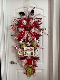 a red and green christmas wreath hanging on the front door with santa's helper sign