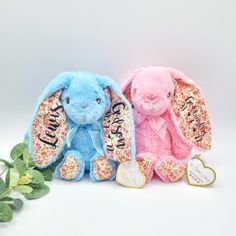 two stuffed animals sitting next to each other on a white surface with flowers in the background