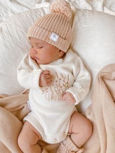 a baby is laying on a bed wearing a knitted outfit and a beanie