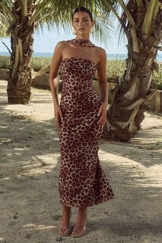 a woman standing in front of palm trees wearing a leopard print dress