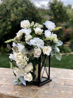 a bouquet of white flowers sitting on top of a wooden table in front of some bushes