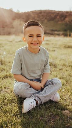 a young boy sitting in the grass smiling