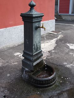 a water fountain on the side of a road with a red building in the background