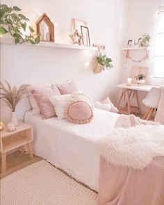 a bedroom with white walls and lots of pillows on the bed, along with plants