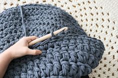 a hand holding a crochet hook on top of a blue knitted blanket