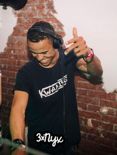 a man wearing headphones standing in front of a brick wall and pointing to the side