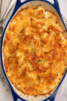 a blue casserole dish with cheese and herbs on the side next to utensils