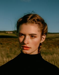 a woman standing in the middle of a field with her hair up and eyes closed